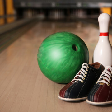 A green bowling ball, ten pin and bowling shoes are on bowling lane.