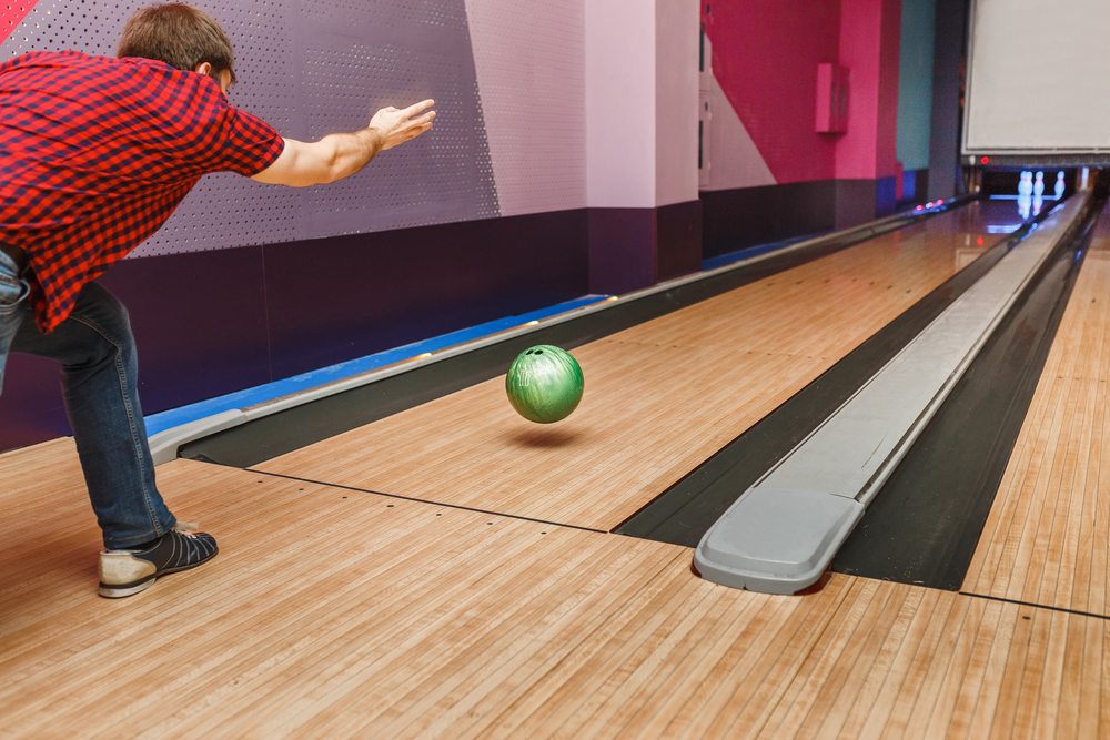 The bowler wears a red shirt and is bowling a red bowling ball and released the ball just in time.