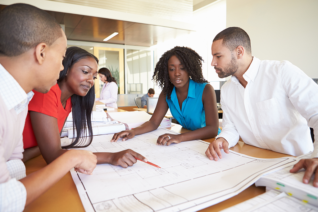 Group Of Architects Discussing Plans In Modern Office In Smart/Casual Dresswear