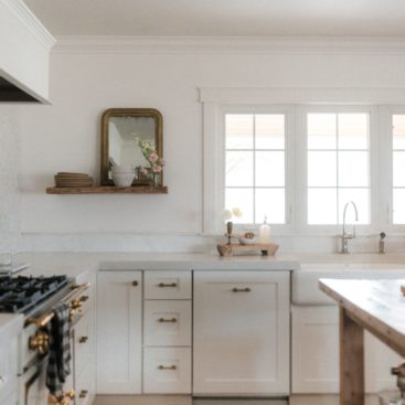 An open white kitchen with white concrete countertops and light filtering through the windows.