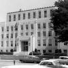 Multistory art deco stone building with carved "Court House city Hall" on the front and flagpole hedges and trees