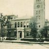 Multistory stone and brick building arched windows columns clock tower by road and trees