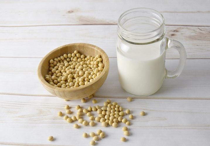 A mason jar of soy milk sits beside dried soy beans against a white wood backdrop