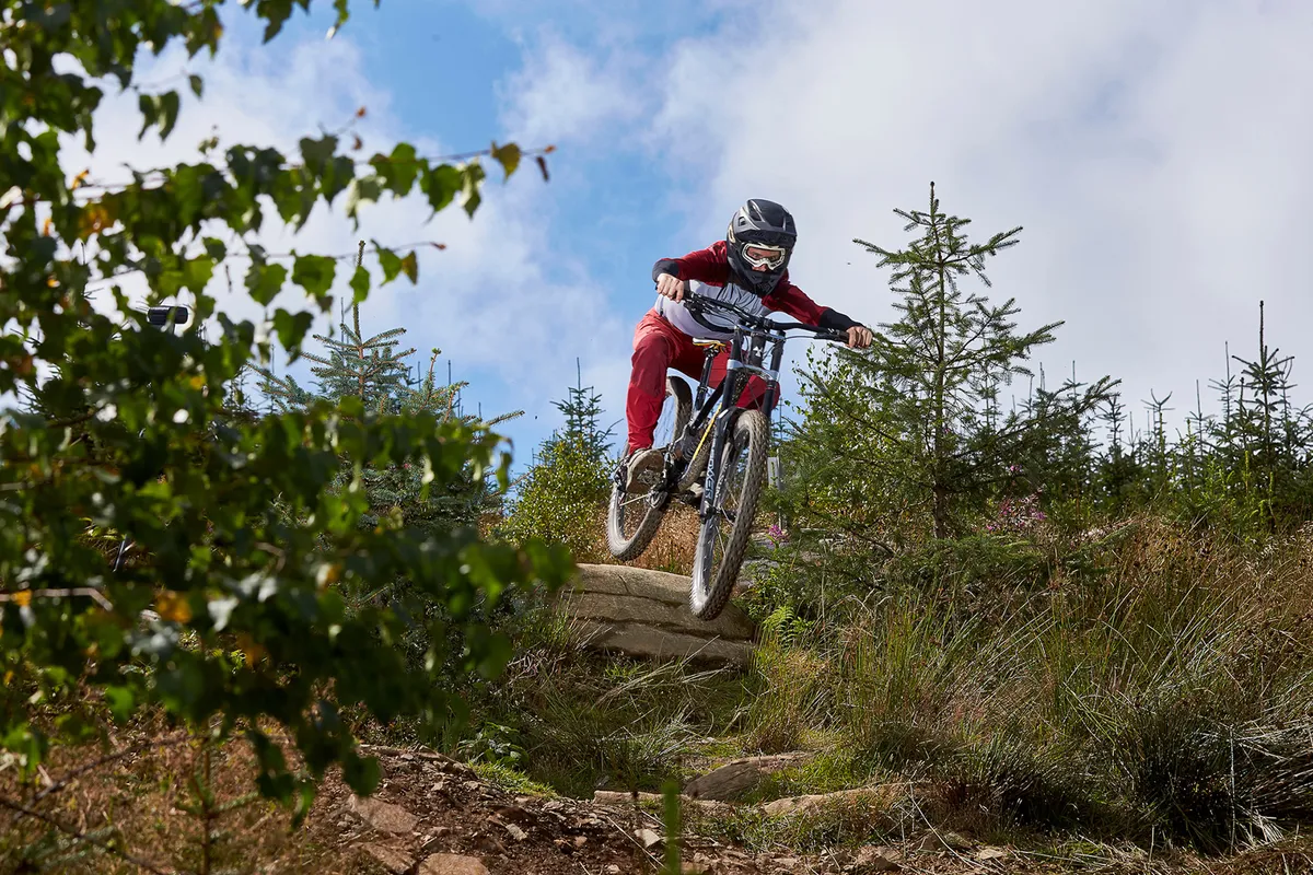 male cyclist wearing red riding black full suspension mountain bike on dirt track