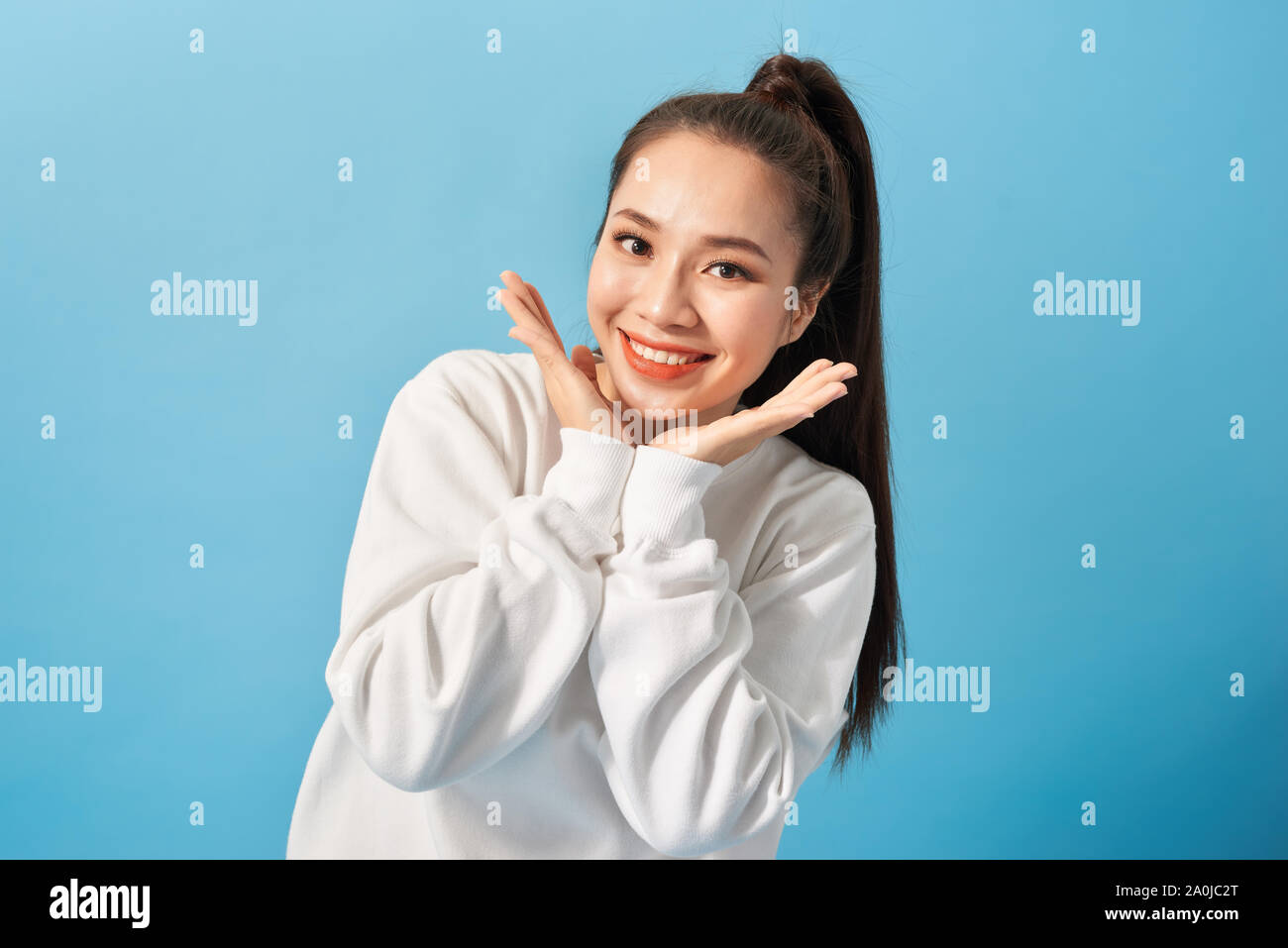 Portrait of joyful carefree adorable adult woman smiling broadly and holding palms near cheeks, being playful and emotive with positive attitude to li Stock Photo