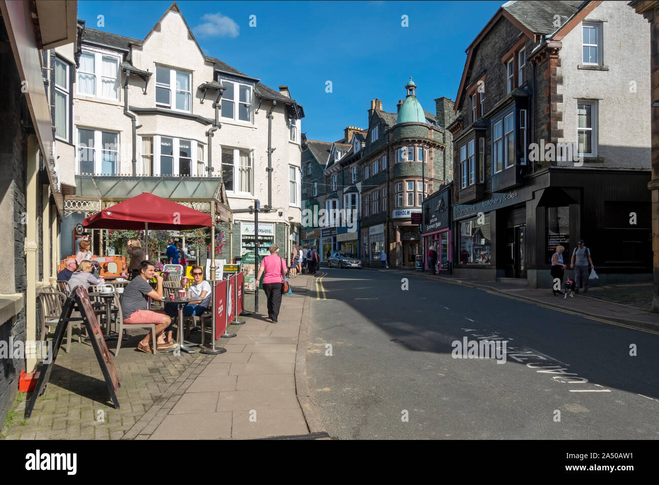 People sitting drinking sat outside cafe in the town centre shops stores in summer Keswick Cumbria England UK United Kingdom GB Great Britain Stock Photo