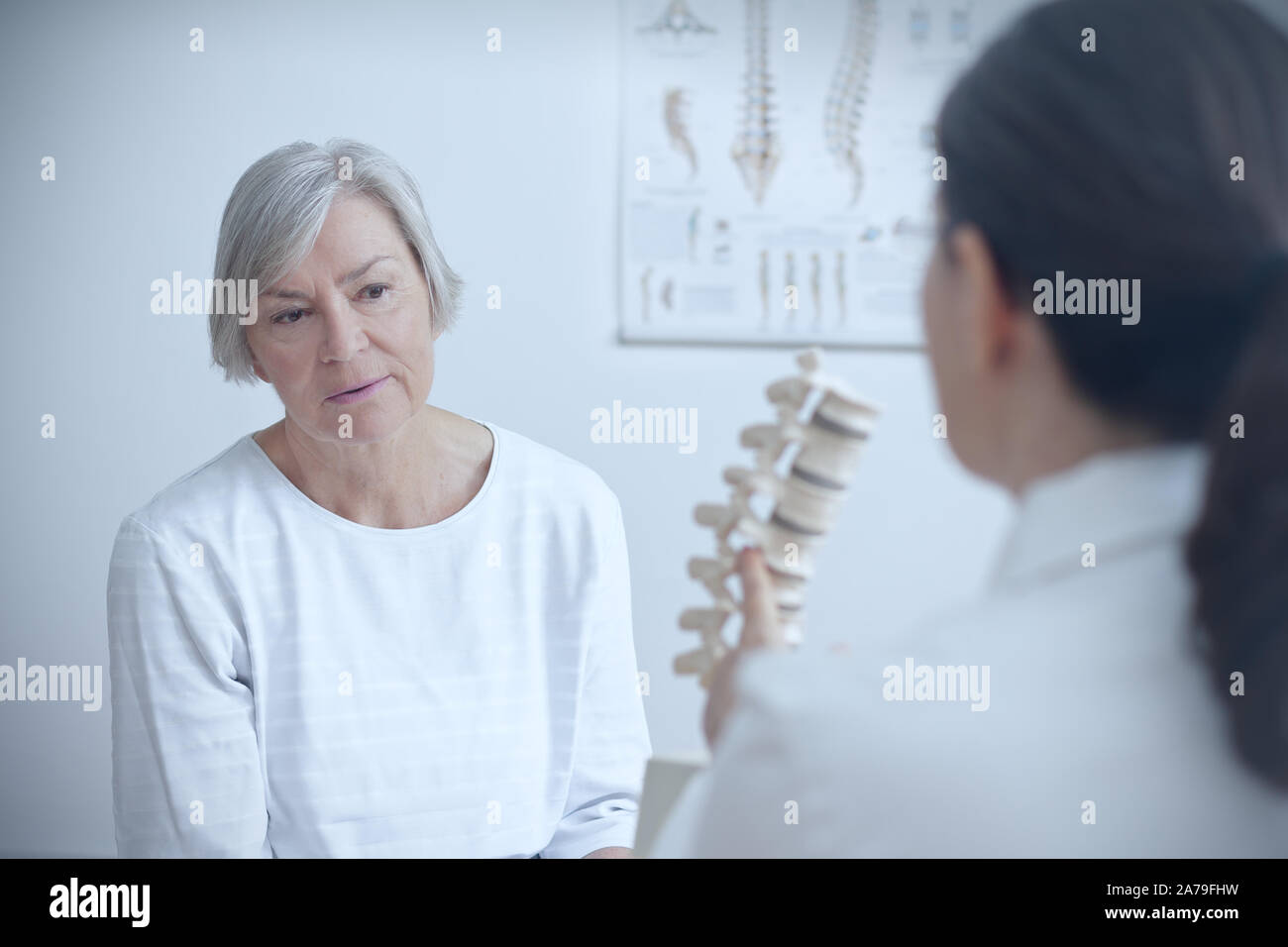 Aging and back pain concept: doctor of orthopedics showing her senior patient a degenerated disk on a backbone model. Stock Photo