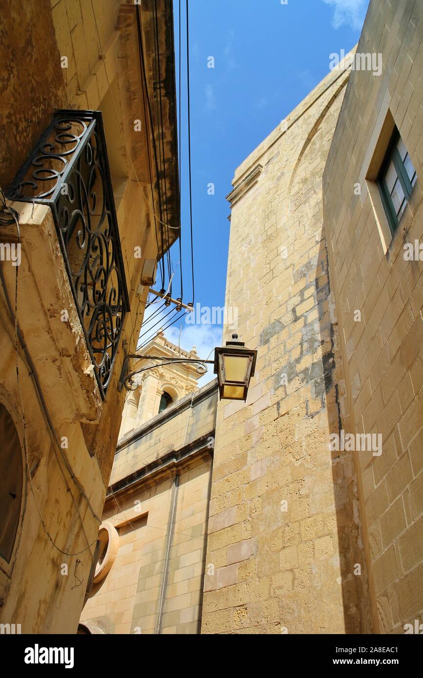 Looking up towards a street lamp and metal balcony strolling through the narrow streets of Valletta old town, Malta. Stock Photo