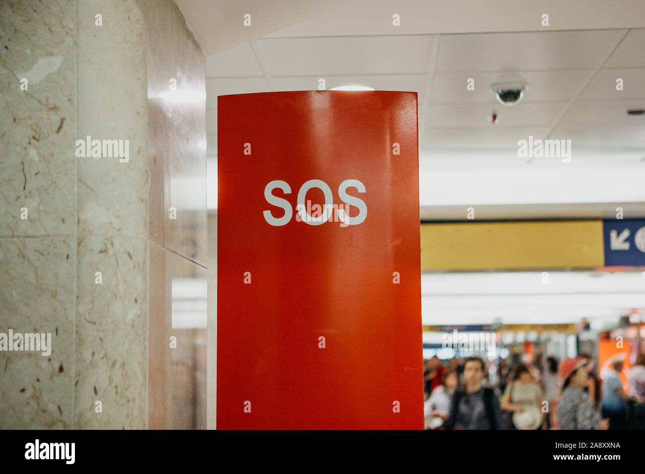 SOS sign on a special stand or booth with a phone for a call at the railway station. Unrecognizable blurry people in the background. Stock Photo