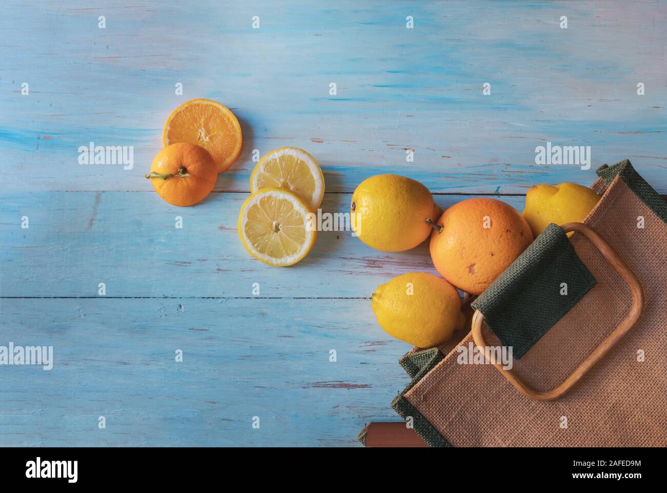 Still life of oranges and lemons coming out of a bag, on a light wooden background Stock Photo