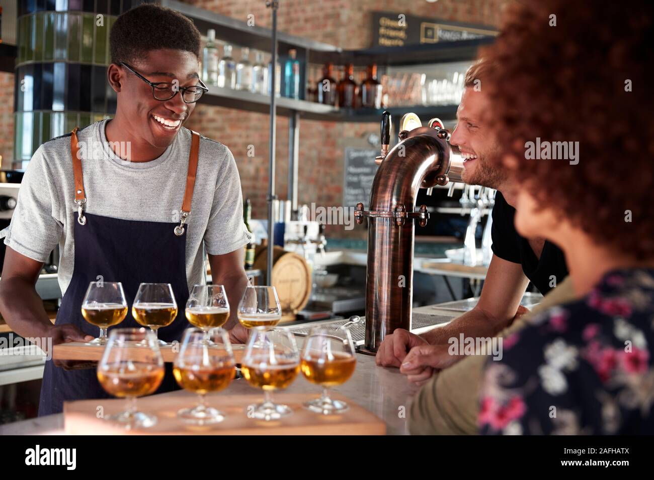 Waiter Serving Group Of Friends Beer Tasting In Bar Stock Photo