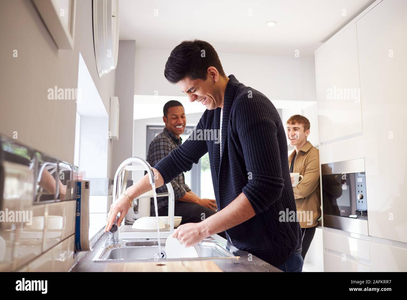 Group Of Male College Students In Shared House Kitchen Washing Up And Hanging Out Together Stock Photo