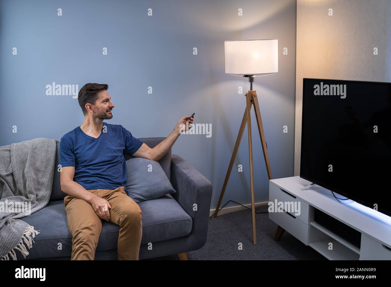 Person Controlling Smart Light With Remote Control Stock Photo