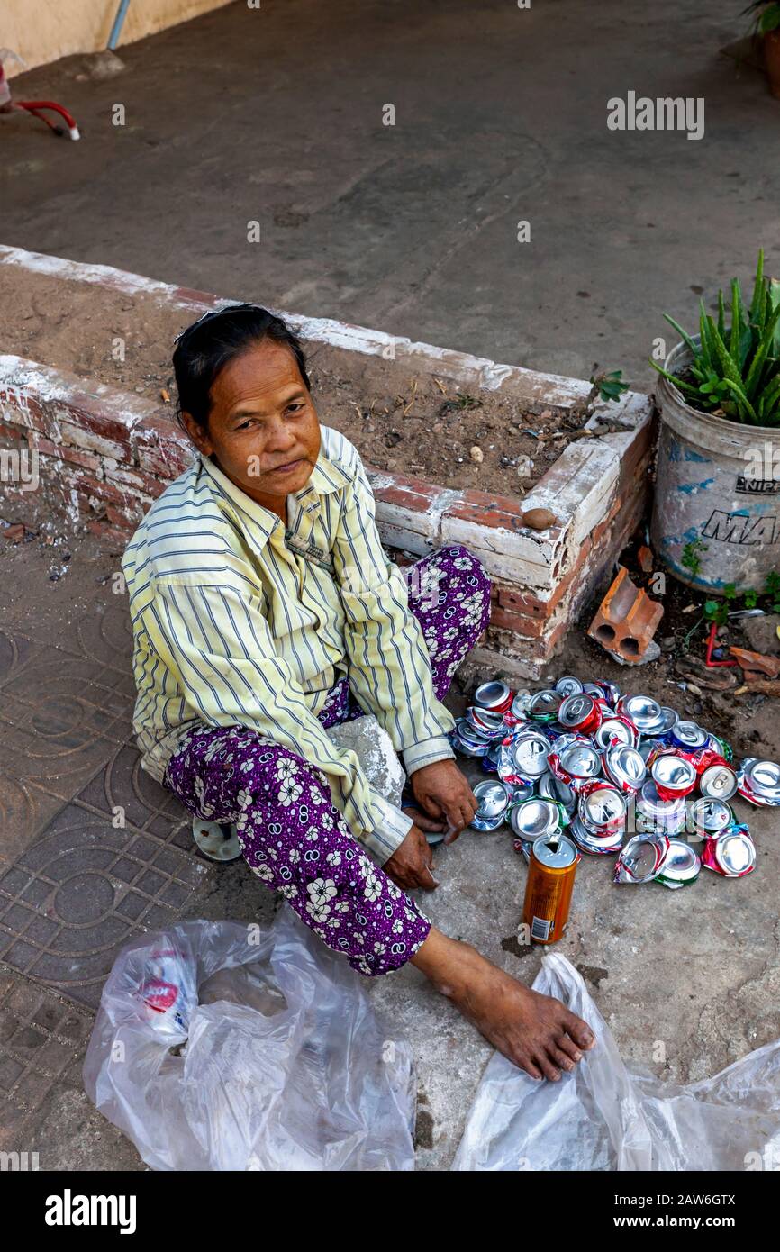 A 50 year old Cambodian woman living in poverty sits on a sidewalk crushing recyclable aluminum cans in urban Kampong Cham, Cambodia. Stock Photo