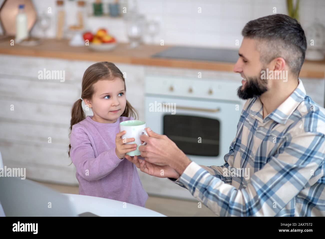 Young dad taking a cup from a little daughter. Stock Photo