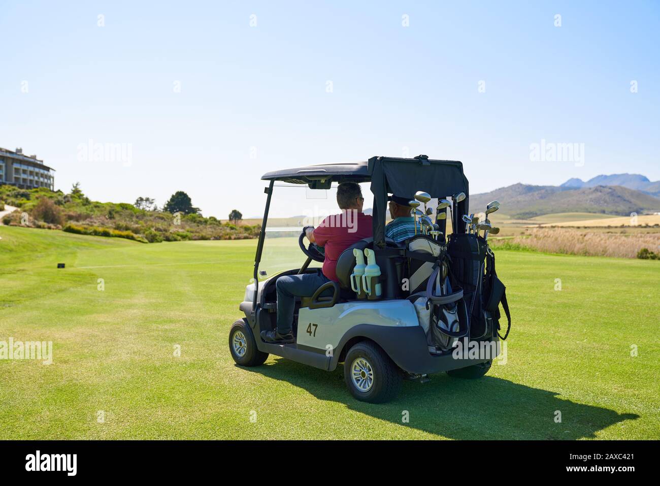 Male golfers driving golf cart on sunny golf course greens Stock Photo