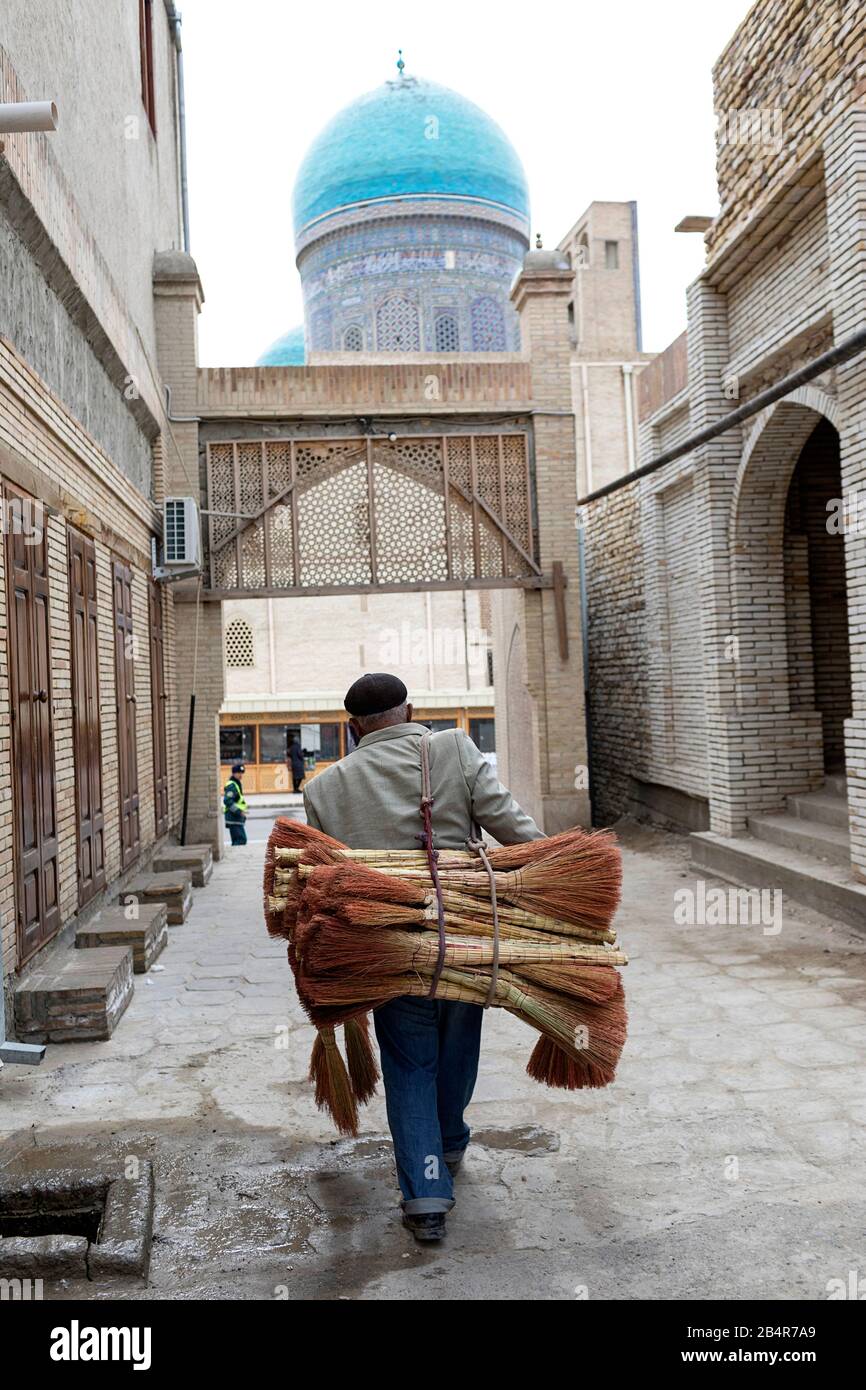 Man carrying pile of brooms for sale on side street in old town of Bukhara, Uzbekistan Stock Photo