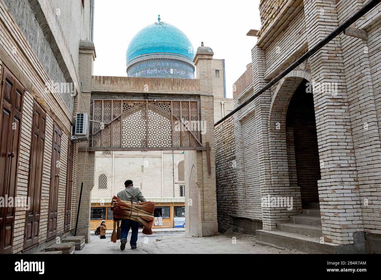 Man carrying pile of brooms for sale on side street in old town of Bukhara, Uzbekistan Stock Photo