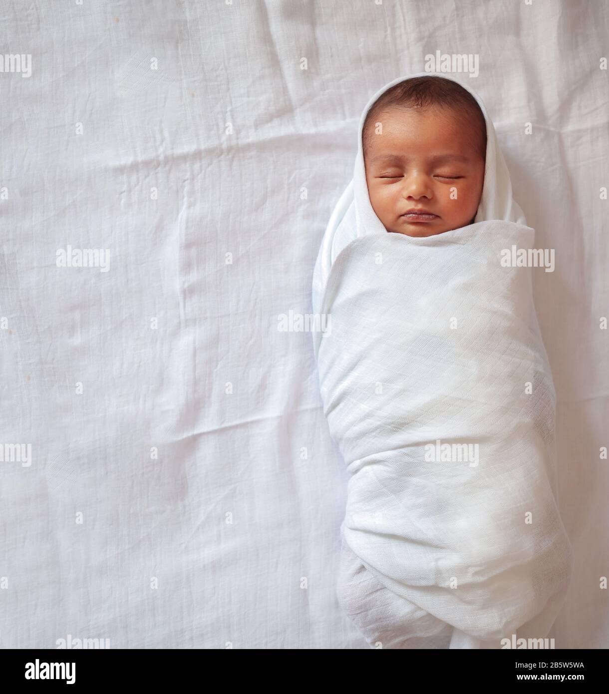 a one month old baby sleeping and swaddled in white cloth lying in white cloth background. Stock Photo