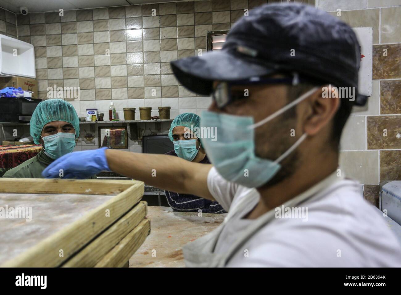 Palestinian workers wearing masks amid coronavirus precautions, bake bread at a bakery, in Rafah in the southern Gaza Strip, on March 10, 2020. Stock Photo