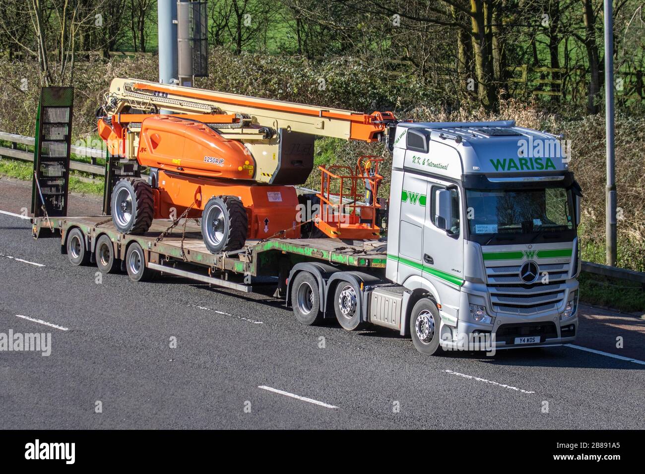 Warisa Haulage delivery trucks, lorry carring JLG Industries lift equipment 1250AJP articulating boom, cherry picker, transportation, truck, cargo carrier, Mercedes Benz 2548 vehicle, European commercial transport, industry, M6 at Manchester, UK Stock Photo