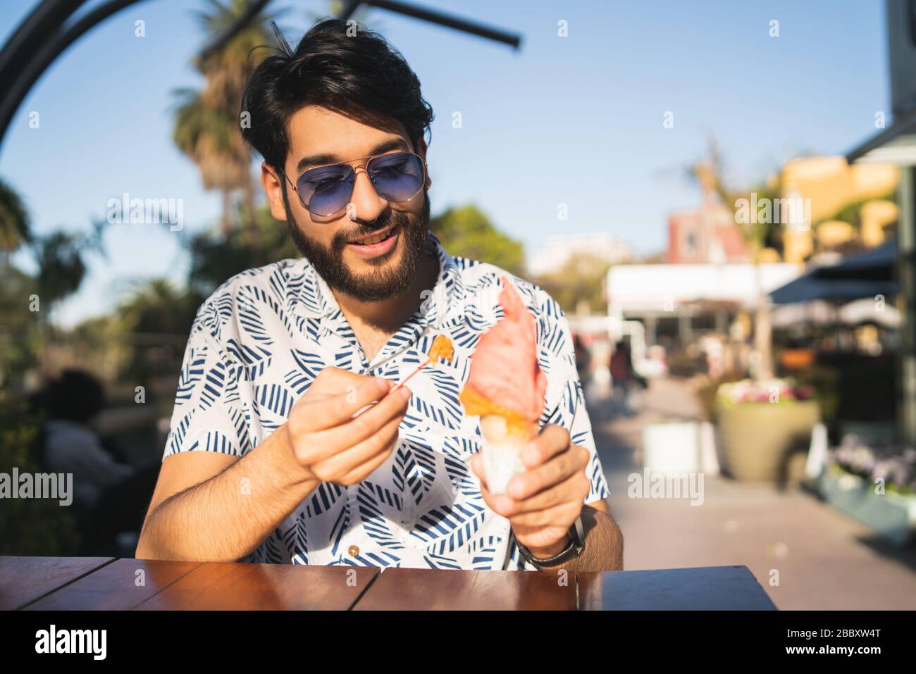 Portrait of young man enjoying sunny weather while eating an ice cream outdoors. Stock Photo