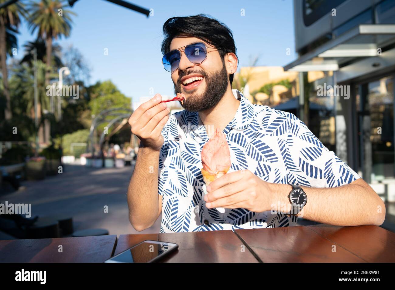 Portrait of young man enjoying sunny weather while eating an ice cream outdoors. Stock Photo