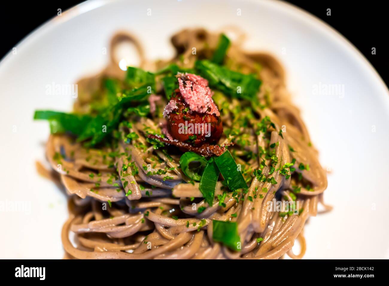 Traditional Japanese white plate with black background and vegetable dish with soba buckwheat noodles, seaweed, green onion negi and umeboshi pickled Stock Photo