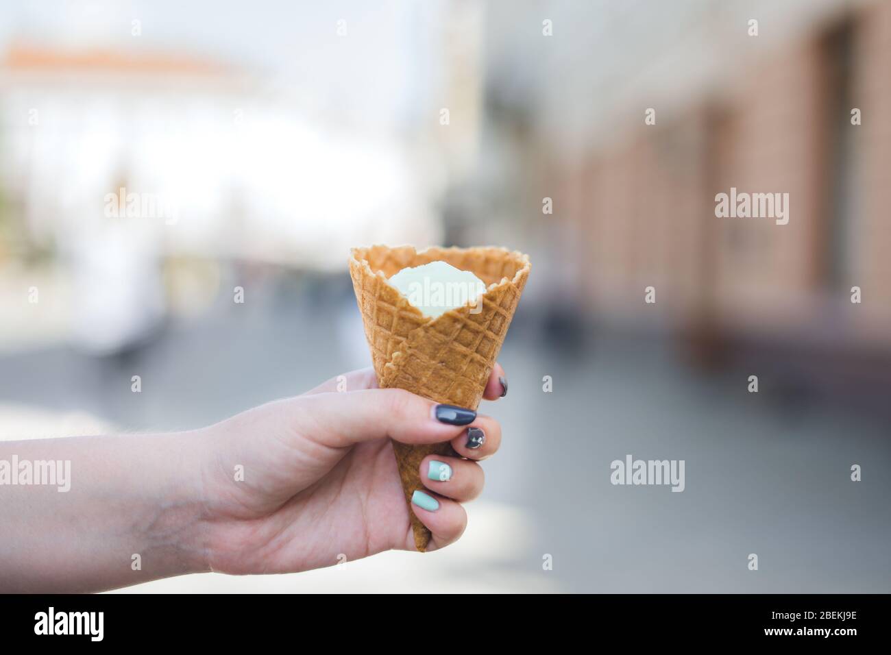 Girl's hand holds vanilla ice cream in waffle cone. Stock Photo