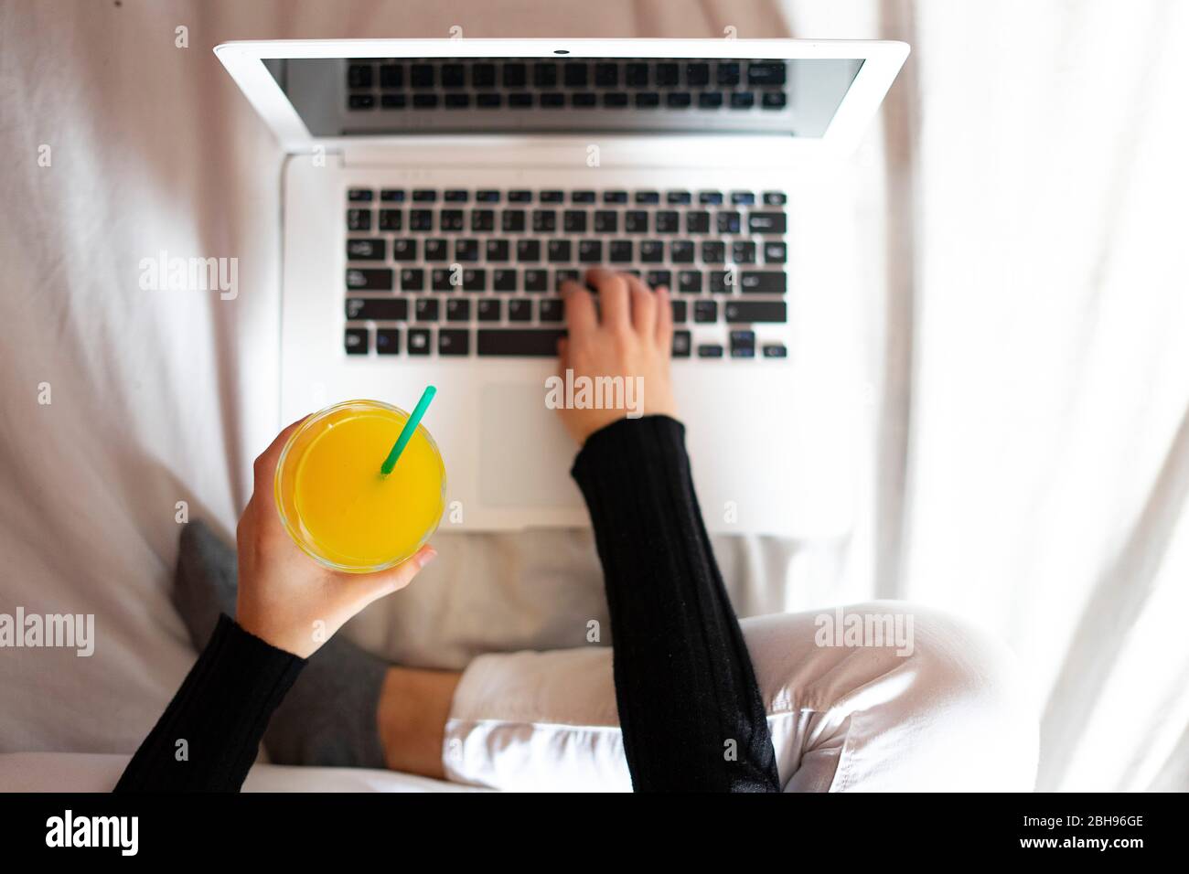 Hand picking up an orange juice next to a laptop. Stock Photo