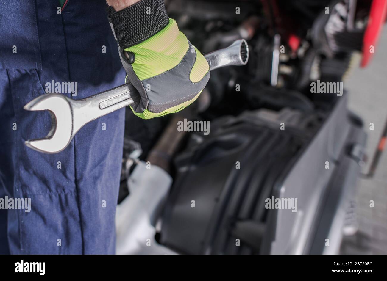 Close Up Of Male Car Mechanic With Coveralls And Gloves Holding Large Wrench At Automotive Repair Shop. Stock Photo