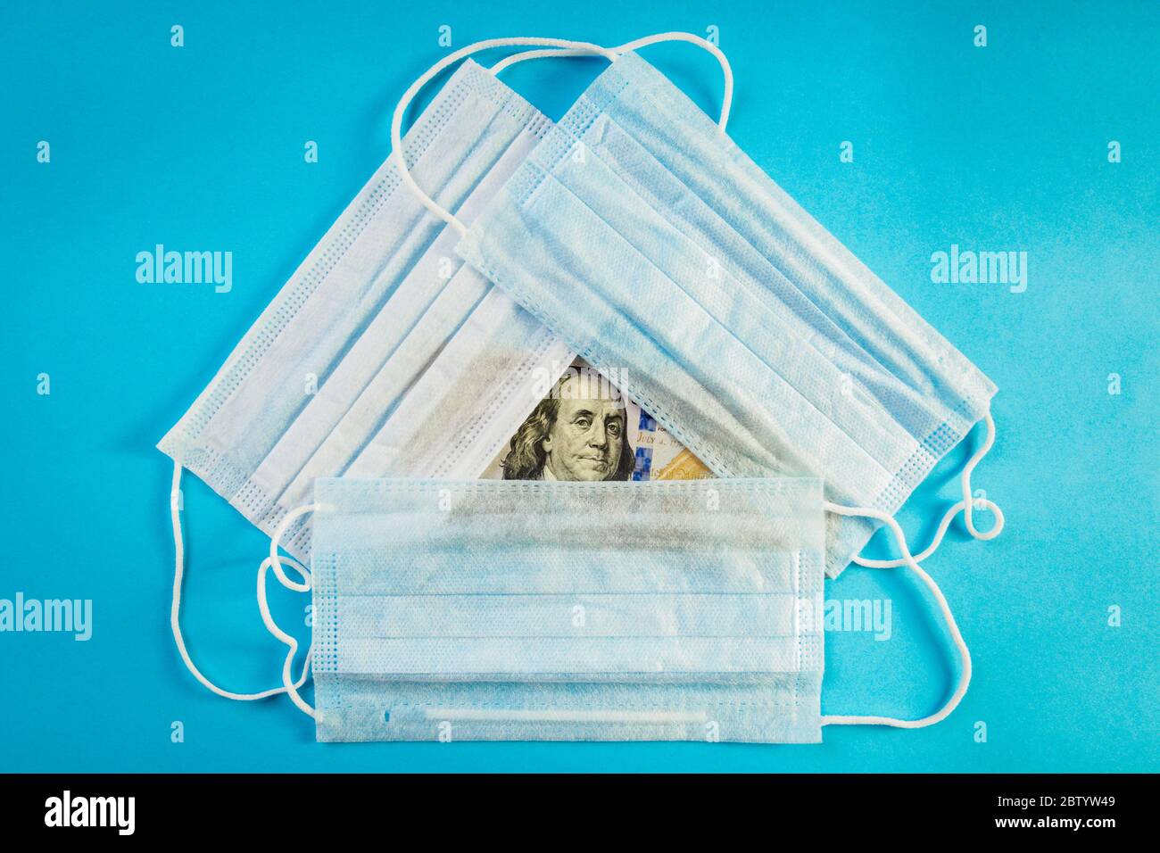 Three medical masks lie on 100 dollars banknote on blue background. Concept of deficit, speculation and sold out of face masks. Top view Stock Photo