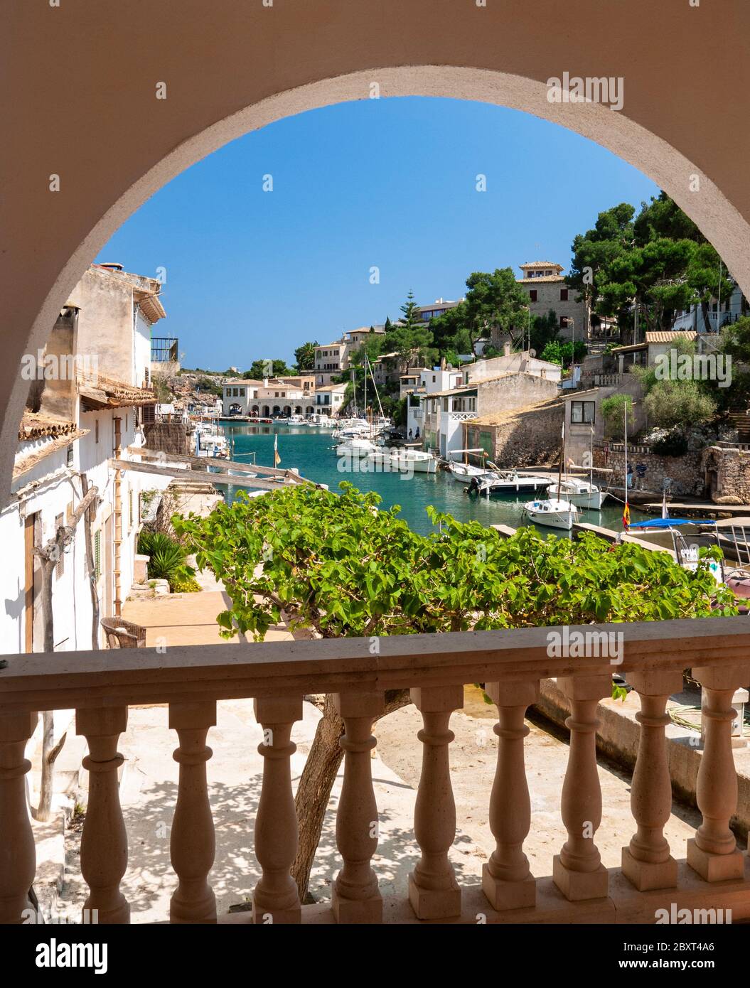 Cala Figuera harbour view framed by vacation villa terrace patio arch through to fishing boats houses and villas, Mallorca Balearic Islands Spain Stock Photo