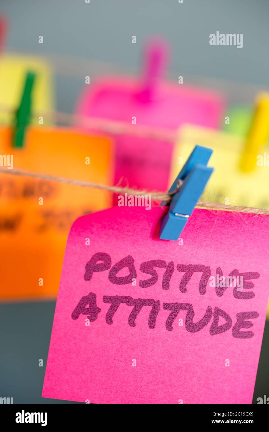 A bright pink sticky note with the text Positive Attitude hung from a clothesline by a blue clothespin. Stock Photo