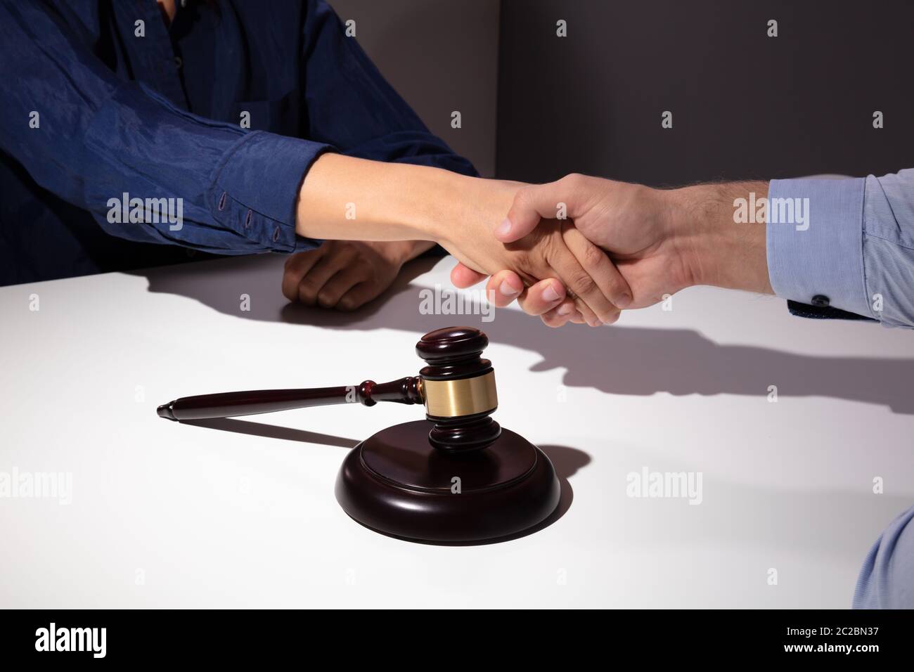 Close-up Of Mallet And Gavel In Front Of Judge Shaking Hands With His Client Stock Photo