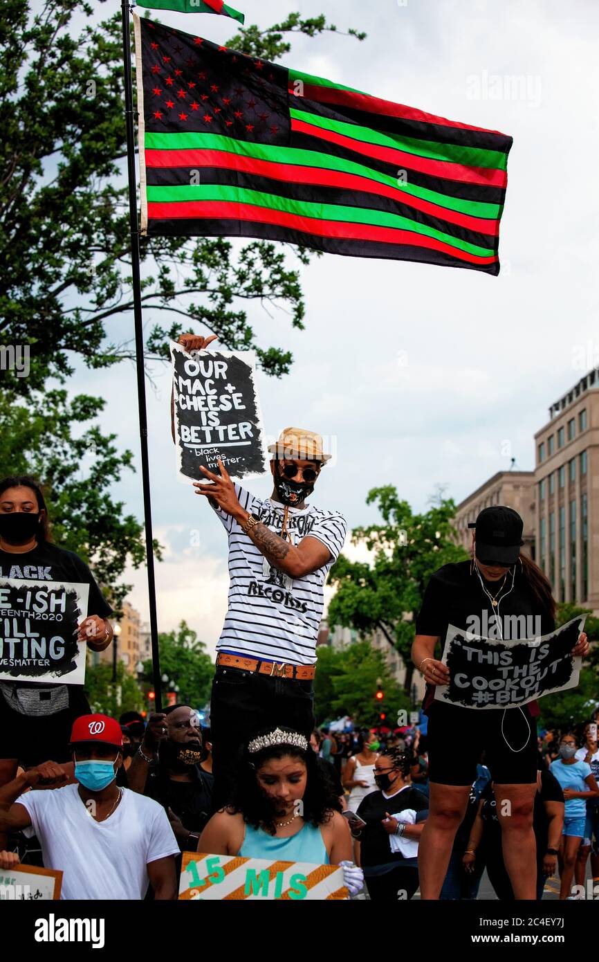 A man holds a sign under a red, green, and black flag during a protest, Juneteenth at Black Lives Matter Plaza, Washington, DC, United States Stock Photo