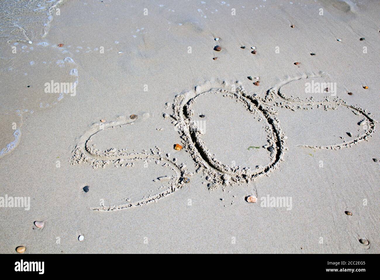 SOS - word drawn on the sand beach with the soft wave. Stock Photo