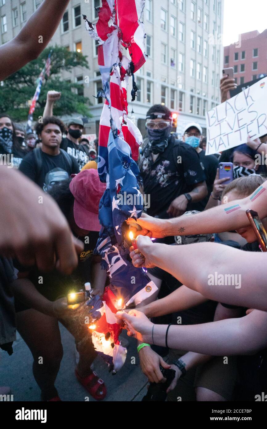 Tulsa, OK, USA. 20th Jun 2020 Protesters reach out with lighters to burn an American flag in protest of a President Donald Trump rally. Stock Photo