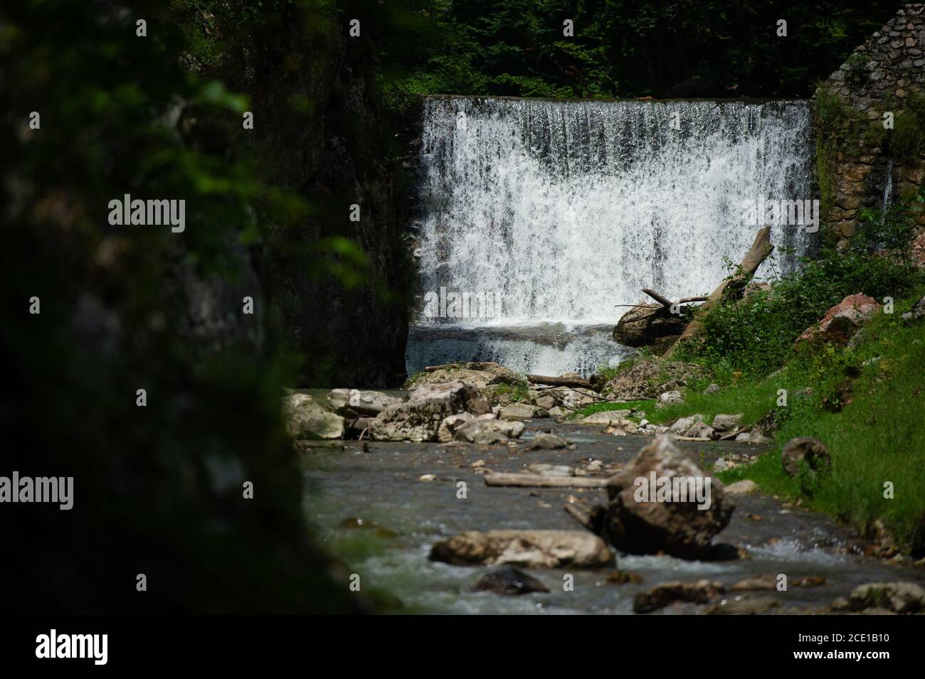 A small rocky river in front of a man-made waterfall. Stock Photo