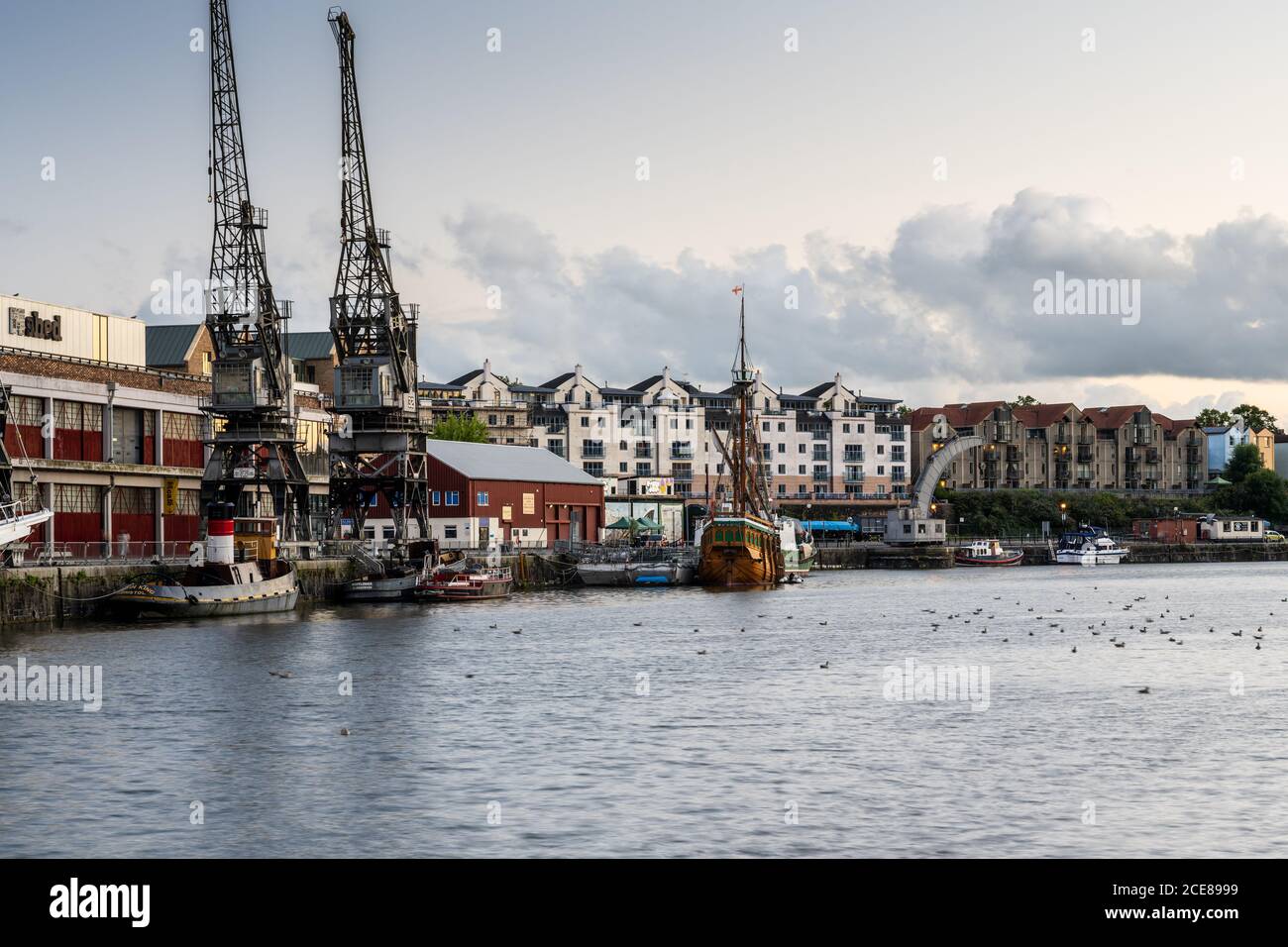 Evening light shines on the M Shed museum, historic vessels and modern apartment buildings on Bristol's regenerated post-industrial Harbourside. Stock Photo