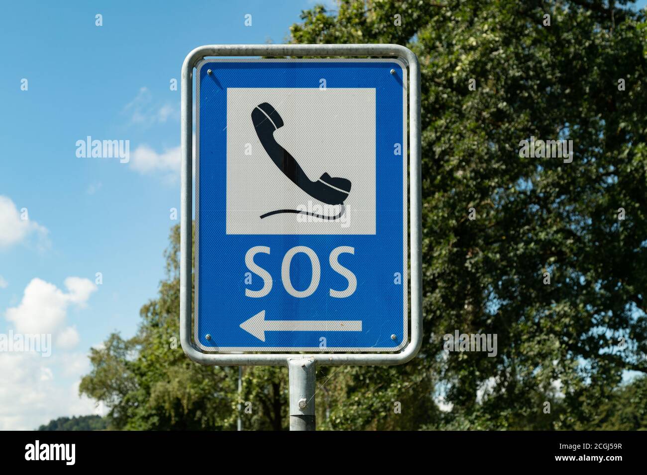 emergency phone sign painted with black phone on white-blue background against blue sky and green forest, emergency calls are important to save lives, Stock Photo