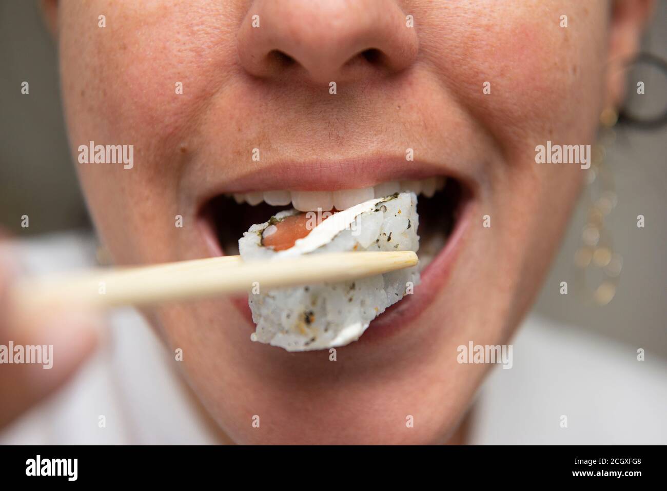 Close up of woman's mouth eating delicious salmon sushi (uramaki). Japanese cuisine. Selective focus. Japan food. Stock Photo