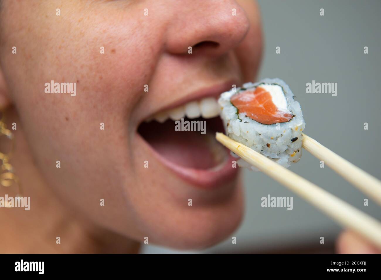 Close up of woman's mouth eating delicious salmon sushi (uramaki). Japanese cuisine. Selective focus. Japan food. Stock Photo