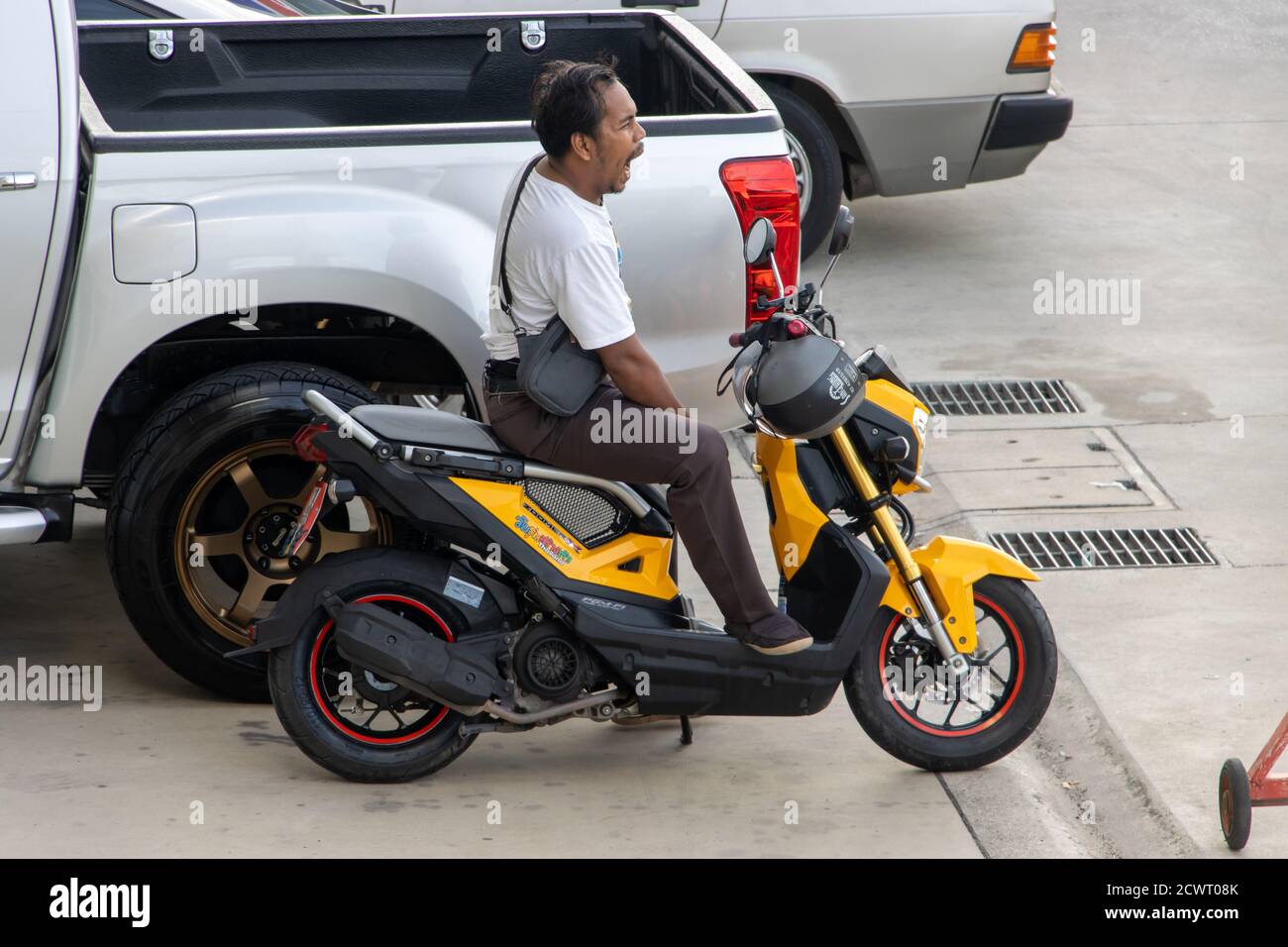 SAMUT PRAKAN, THAILAND, JUN 15 2020, A man is sitting on a parked motorcycle and yawning. Stock Photo