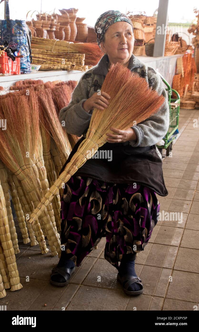 Tashkent, Uzbekistan - May 18, 2018 - Vendor talks to out-of-frame customer to sell her broom Stock Photo