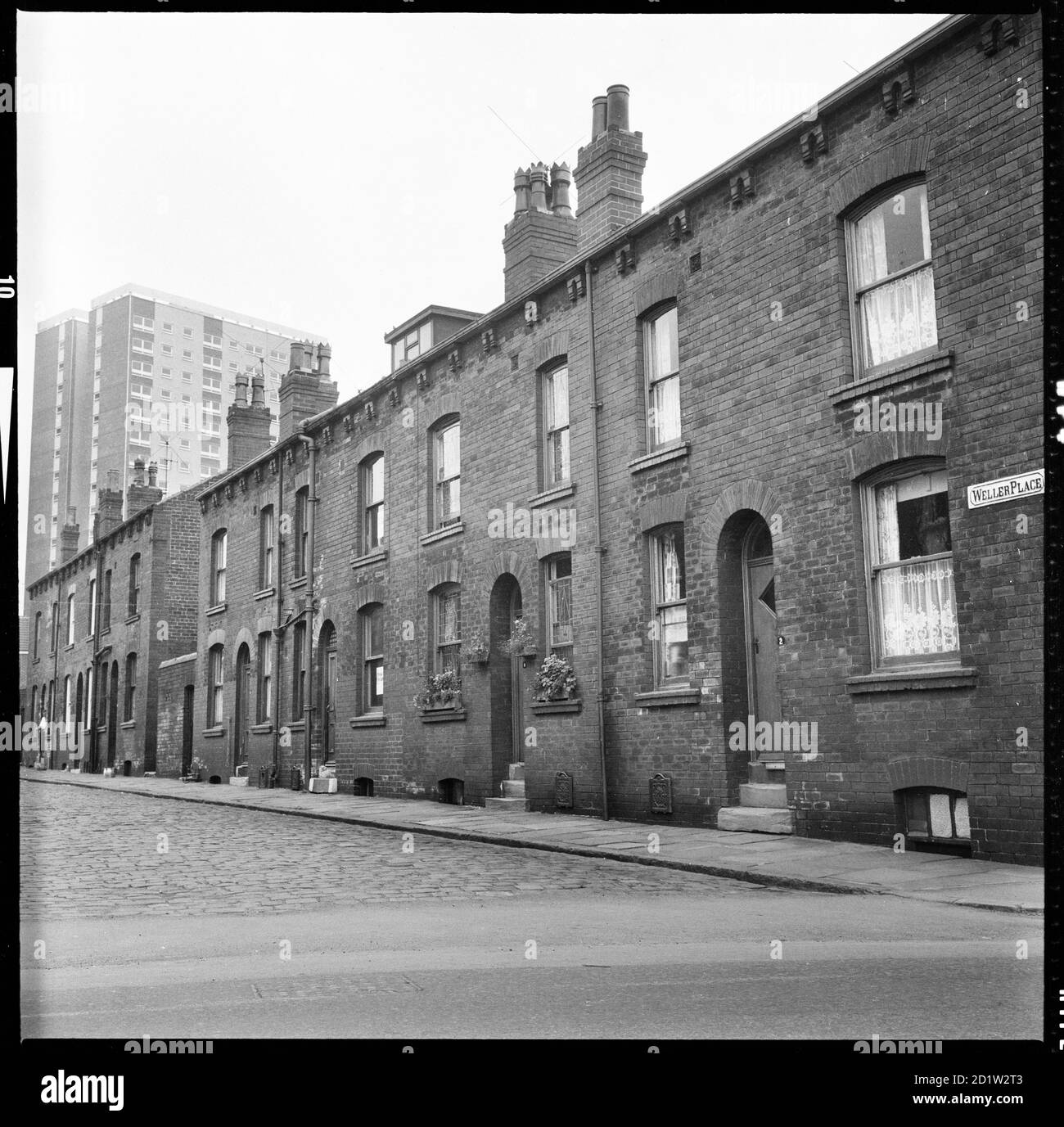 Houses on the south side of Weller Place with number 2 in the foreground and Scargill Grange tower block in the background, Burmantofts, Leeds, West Yorkshire, UK. Stock Photo