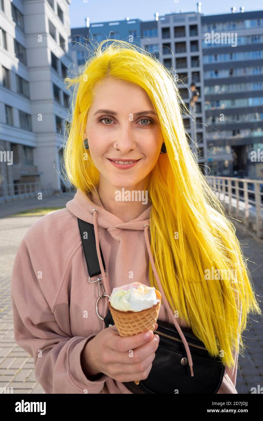 Young woman eating ice cream cone while standing on street in city during sunny day Stock Photo