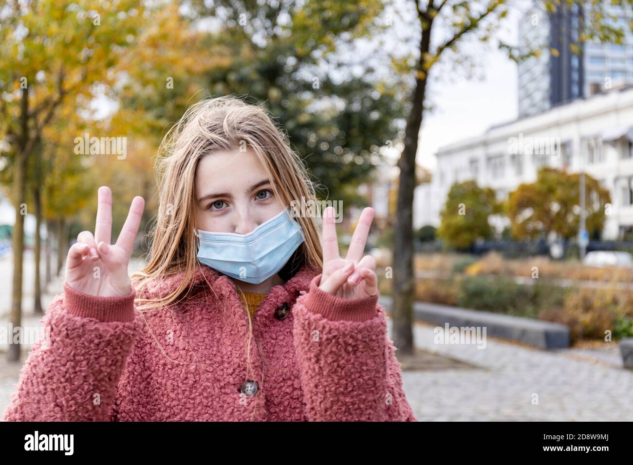 Girl wearing face mask for corona virus with positive attitude. Giving peace sign with two hands. Stock Photo