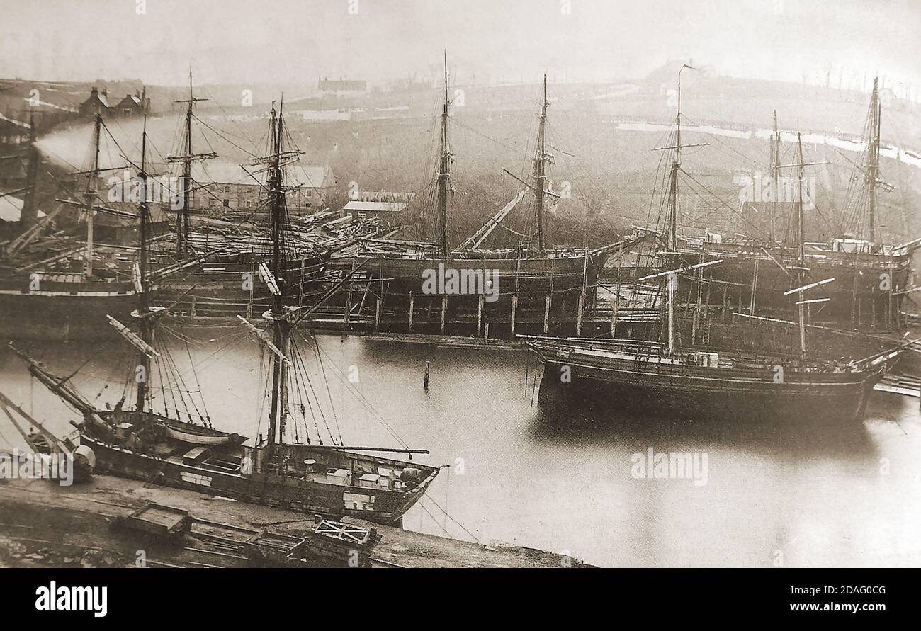 A rare & unusual old photograph showing sailing ships being built or repaired at the Whitehall shipyard on the river Esk at , Whitby, North Yorkshire (UK) during the Victorian period. White Hall, or Whitehall  (still standing in 2020) was the home of the shipyard owner, Thomas Turbull. The two gable ends of the building (top left) can be seen in the picture. A collier (coal ship) selling coal to the public is moored on the other side of the river close to where the Co-op store carpark and marina are situated today (2020) Stock Photo