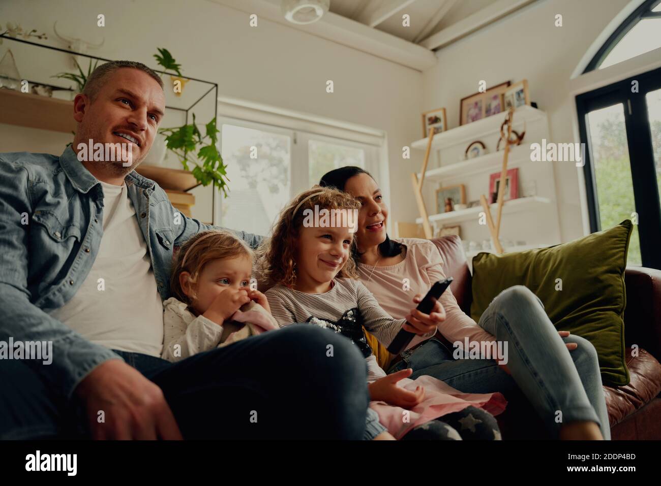 Smiling young parents sitting together with daughter controlling remote control at home Stock Photo